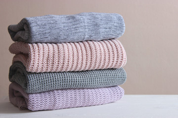 A pile of warm sweaters on a wooden table on a light background. Autumn and winter clothes.