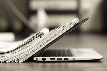 Open laptop and stack of newspapers. Daily journals with news and personal computer. Concept for...