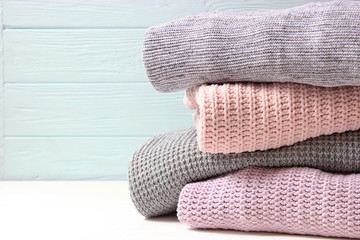 A pile of warm sweaters on a wooden table on a light background. Autumn and winter clothes.