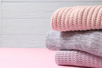 A pile of warm sweaters on a wooden table on a light background. Autumn and winter clothes.