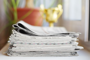 Newspapers stacked in pile and golden trophy cup, concept for winning award in business