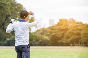 Man golf player swing shot on course in the park with warm sunlight, leisure or sport concept.Man playing golf on a golf course in the sun