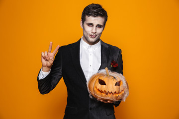 Pretty zombie man showing peace gesture and holding pumpkin in web