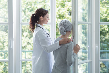 Doctor in white uniform helping kid with cancer during treatment