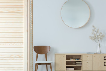 Round mirror above wooden chair and cabinet in minimal anteroom interior with decor. Real photo