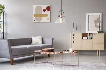 Real photo of a modern living room interior with a sofa, copper coffee tables and wooden cupboard