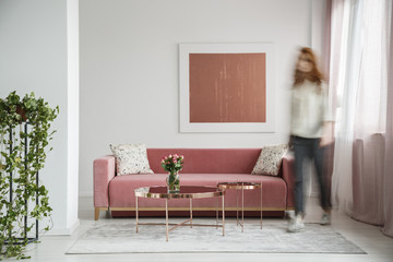 Blurred woman walking in a feminine living room interior with a sofa, coffee table and painting - obrazy, fototapety, plakaty