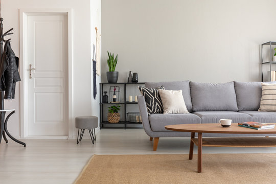 Wooden table on carpet in front of grey sofa in minimal living room interior with door. Real photo