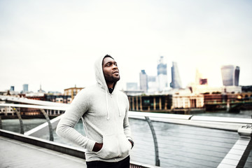Black man runner walking on the bridge in a city, hood on head.