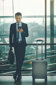 An Asian Businessman Is Using A Smartphone To Get In Business While Waiting For A Trip In The Airport.