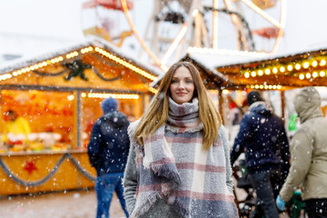 Obraz na płótnie Canvas Beautiful young woman having fun on traditional German Christmas market during strong snowfall.