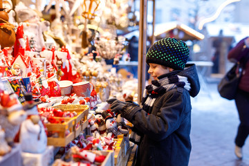 Little cute kid boy selecting decoration on Christmas market. Beautiful child shopping for toys and decorative ornaments