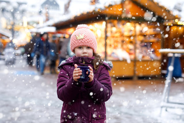 Little kid girl with hot chocolate on Christmas market