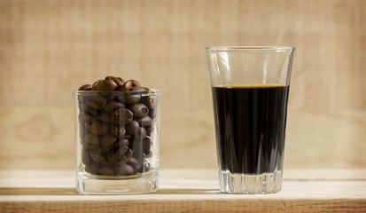 Black coffee in glass and Coffee beans in glass on wooden background.