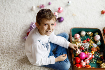 Fototapeta na wymiar Beautiful kid boy and colorful vintage xmas toys and ball in old suitcase. Child decorating Christmas tree
