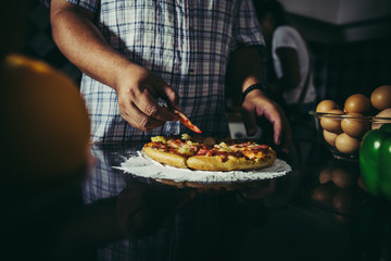 Close up of woman hand put topping on homemade pizza.