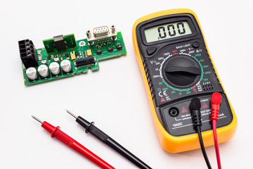 Electric multimeter with red and black probe, display indicating zero, with printed circuit board....