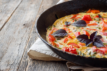 Omelet with vegetables in a pan close-up. Wooden background, top view horizontal