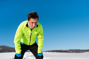 A portrait of senior man standing after the run in winter nature.