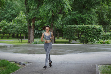 Fototapeta na wymiar Young woman jogging down a path in a green park.