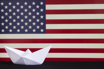 Happy Columbus Day, the great National USA holiday. Celebrated on the second Monday in October. White paper boat over blurred American flag. Stripes and stars.