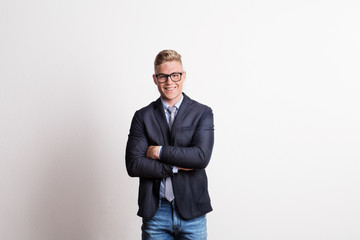 Portrait of a confident young man with glasses in a studio, wearing suit and tie.