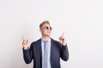 Portrait of a confident young man with sunglasses in a studio, wearing suit and tie.