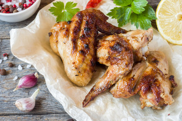 Chicken wings baked on grill with fresh herbs, lemon on wooden background.