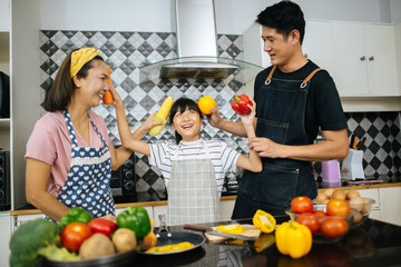 Cute girl help her parents are cutting vegetables and smiling while cooking together in kitchen at home.