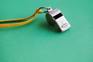 Vintage silver whistle on green paper background. Referee trainer sport competition sound...