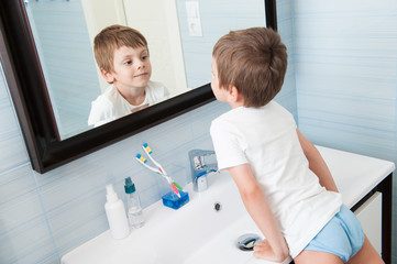 handsome healthy small caucasian boy watching at his reflection in mirror in bathroom