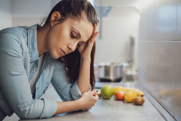 Sad girl leaning on the kitchen countertop and looking down
