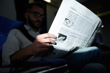 Close up of unrecognizable man holding business newspaper  while reading in plane, shot with flash,...