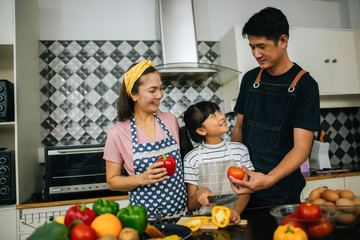 Cute girl help her parents are cutting vegetables and smiling while cooking together in kitchen at home.