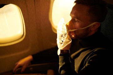 Side view portrait of mature man wearing oxygen mask in plane, copy space