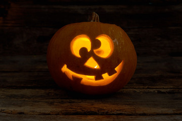 Funny Jack-O-Lantern with glowing candle. Halloween pumpkin face with burning candle on dark background. Halloween holiday celebration.