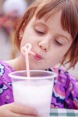 Cute little child girl drink milk cocktail. Happy childhood concept.
