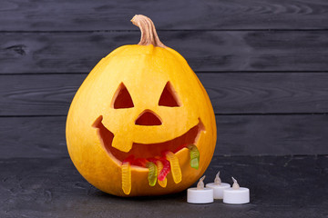 Funny Halloween pumpkin on dark background. Halloween pumpkin with jelly worms in mouth, funny Jack. Halloween funny decoration ideas.