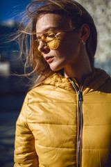 A young European woman, traveling, with long blond hair, wearing a yellow jacket, yellow sunglasses...