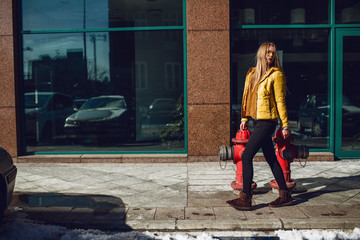 Obraz na płótnie Canvas A young European woman, traveling, with long blond hair, wearing a yellow jacket, yellow sunglasses walking down the city center street, street shooting. Even light.