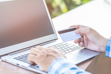 Man's hands holding a credit card and using laptop for online shopping.