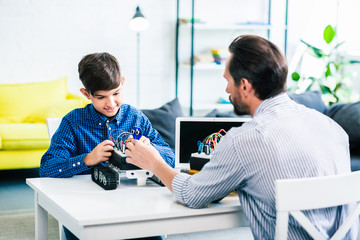 Cheerful schoolboy constructing robot with his father