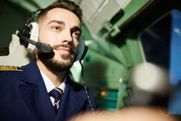 Head and shoulders portrait of handsome pilot in cabin of modern airplane, copy space
