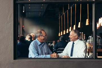 Two mature business men handshake at cafe