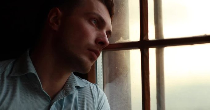 Loneliness in the mountains. Handsome young man leans to the window and closes his eyes looking at the evening mountain landscape outside