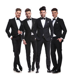 four elegant young men in tuxedos standing together