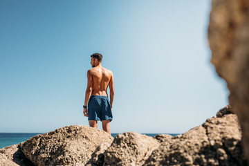 Fototapeta premium Man standing on top of rocks looking at the sea