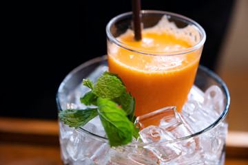 A glass of mixed orange and carrot juice in a jar of ice with mint leaves