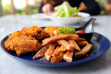Closeup image of a plate of fried chicken and french fries with a woman eating salad in the restaurant