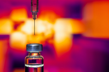 A syringe with the needle point to the vaccine vial on the colorful abstract background